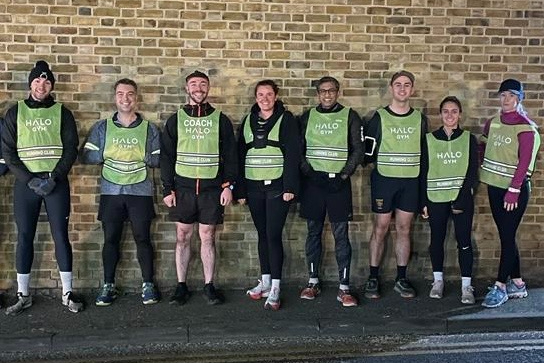 Halo Gym Running Club group photo with coach and members wearing green club vests, standing in front of a brick wall.