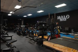 Halo Gym floor with free weights, weightlifting platforms, strength machines, and functional training equipment in a well-lit workout area.