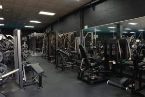 Weight training area at Halo Gym with benches, resistance machines, free weights, and mirrored walls for form checks
